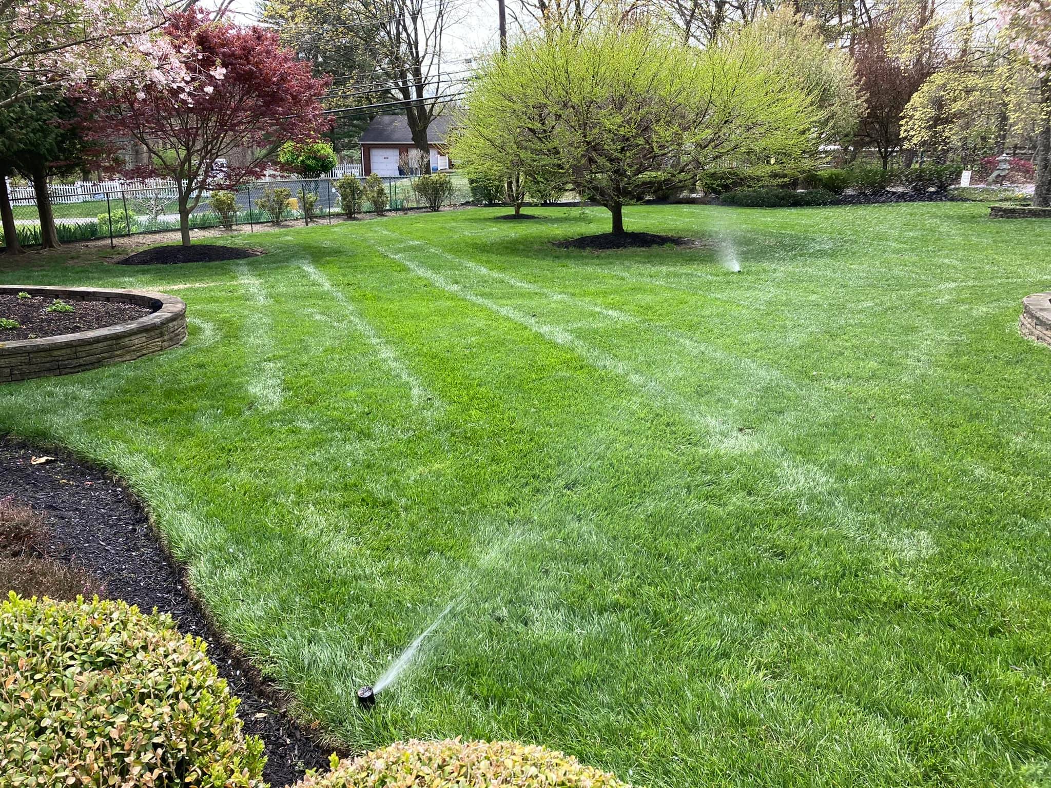 An active multi-zone automatic lawn sprinkler system watering a beautifully manicured green grass yard.