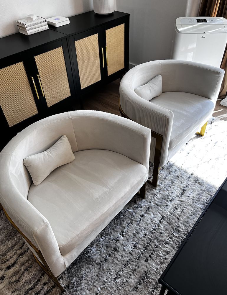A stylish seating area with two upholstered accent chairs placed on a textured rug, beside a black cabinet with woven panels, creating a modern, clean, and organized interior space.