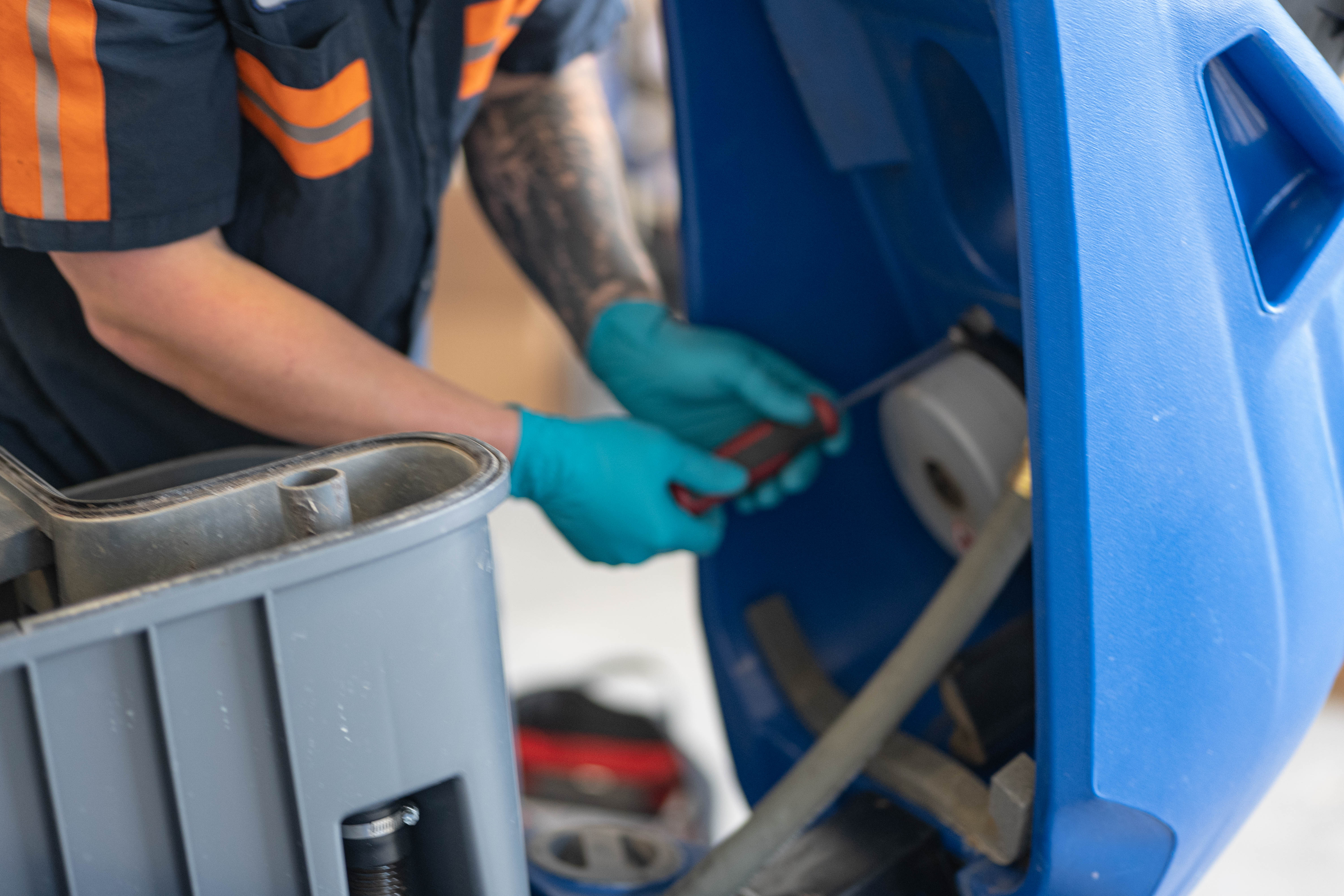 A certified WaySolutions technician carefully uses hand tools to service the internal vacuum motor of a blue Kärcher Chariot stand-on floor scrubber. Providing specialized commercial cleaning equipment repair in Layton, Utah, our experts ensure your facility's machines maintain optimal suction and performance with precise, hands-on maintenance.
