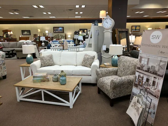 Styled living room furniture display featuring a white sofa, patterned accent chair, coffee table, lamps, wall d&eacute;cor, and home accessories inside Neill&rsquo;s Homestore.