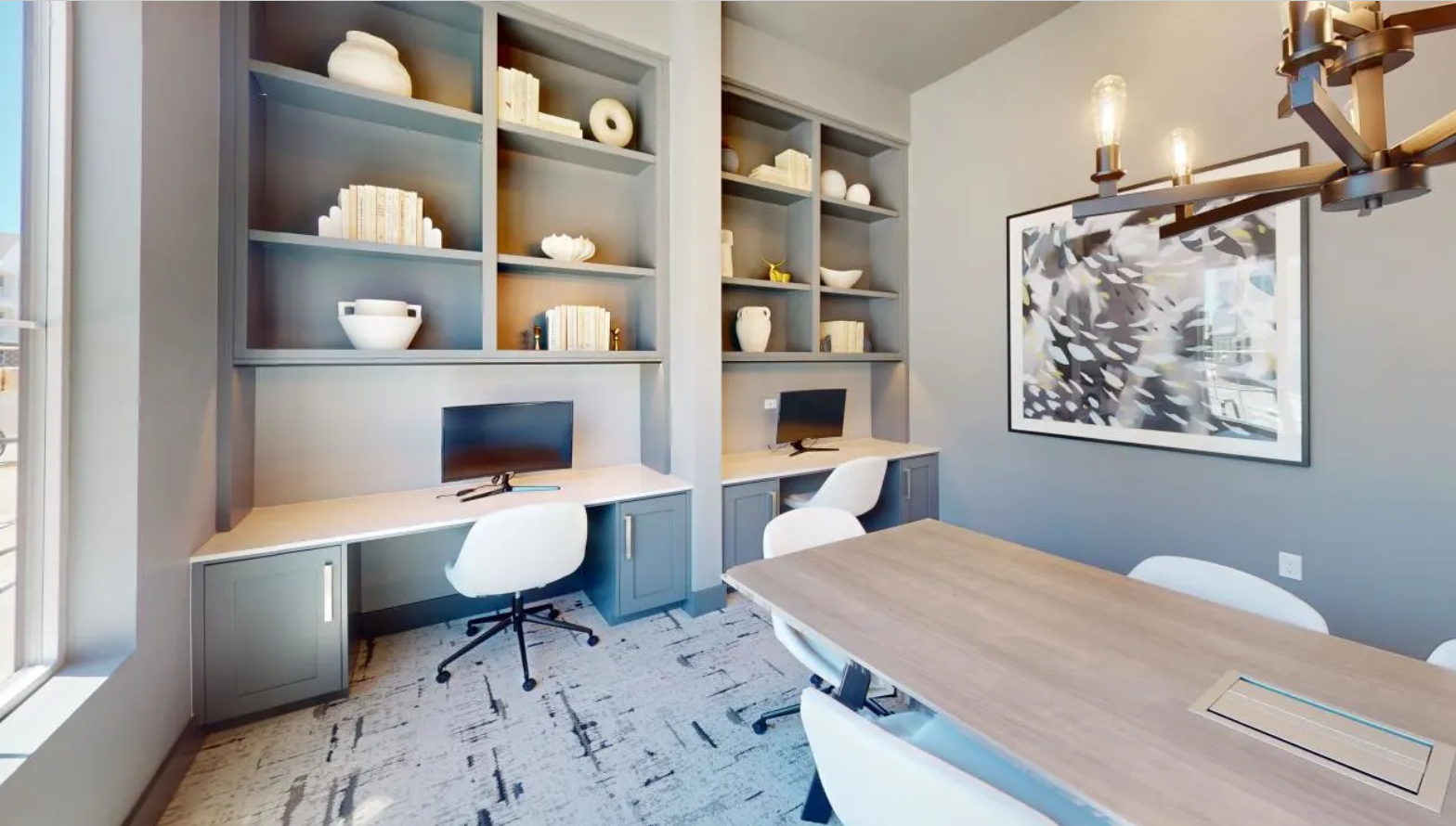 Resident business center with a large conference table, built-in shelving in front of two desks with a divider, and computers