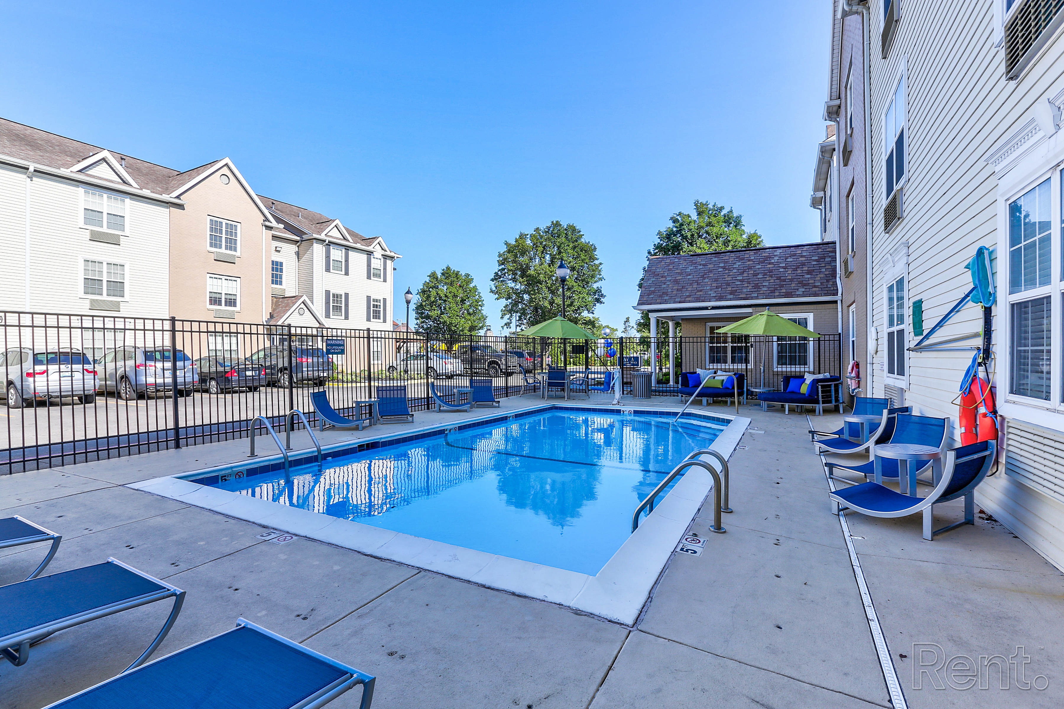 A swimming pool with lounge chairs and umbrellas is surrounded by apartment buildings at AVIA North Shore in Jeffersonville, IN