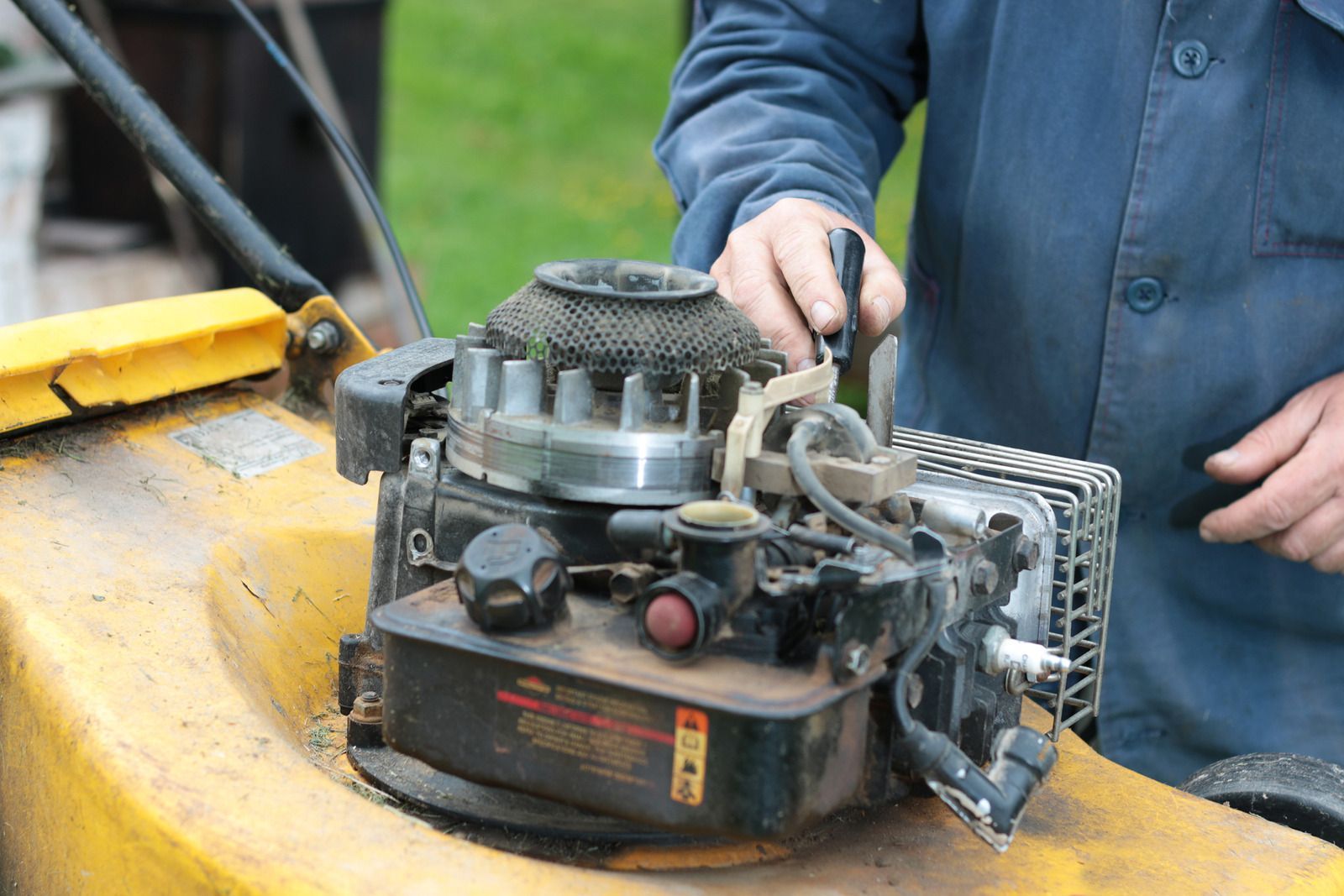 A technician works on a small engine mounted on a yellow lawn mower, adjusting components near the carburetor and air filter. The image reflects routine maintenance or repair of outdoor power equipment.