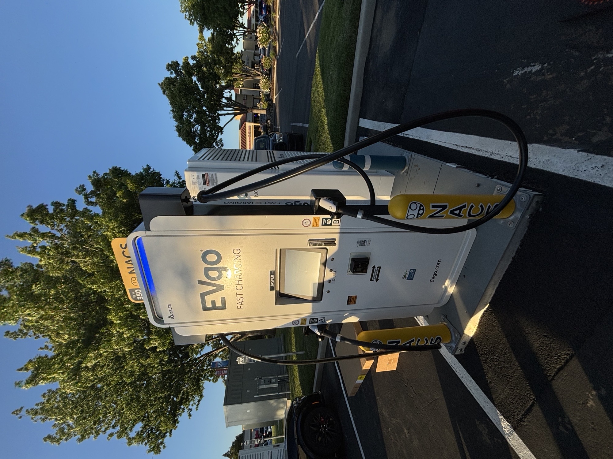 NACS EVgo fast charging unit installed in marked parking space at a public charging station, with EVgo logos on the charger, and yellow protective bollards around the unit