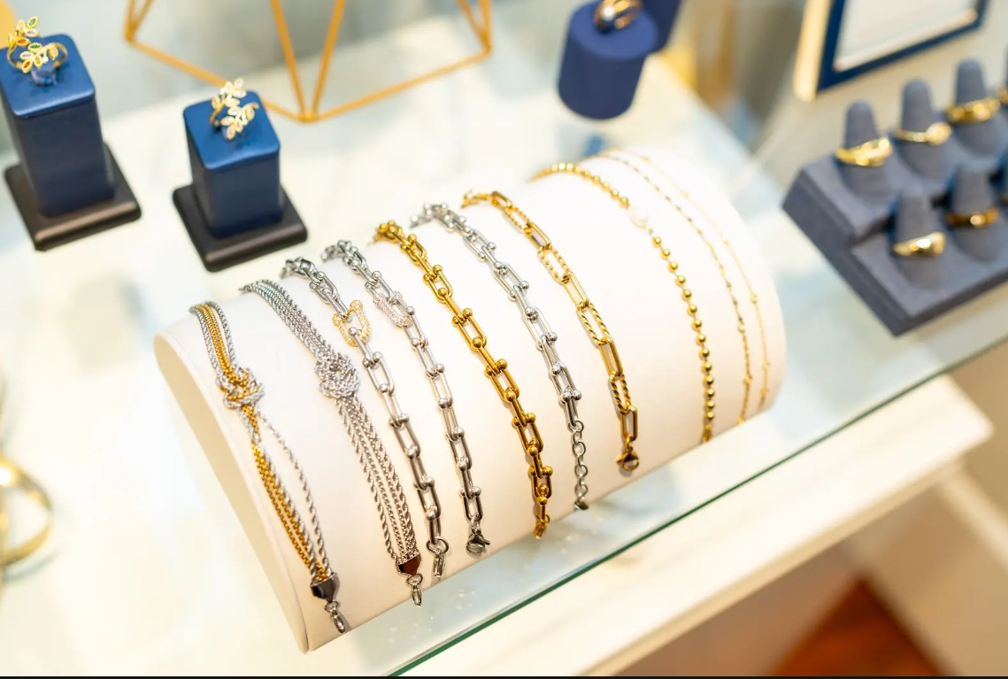 Gold-tone and silver-tone chain bracelets line white jewelry stand at Eliana Curated. Discover delicate bead designs, bold links, and layered styles for everyday wear in Old Town Alexandria, Virginia.