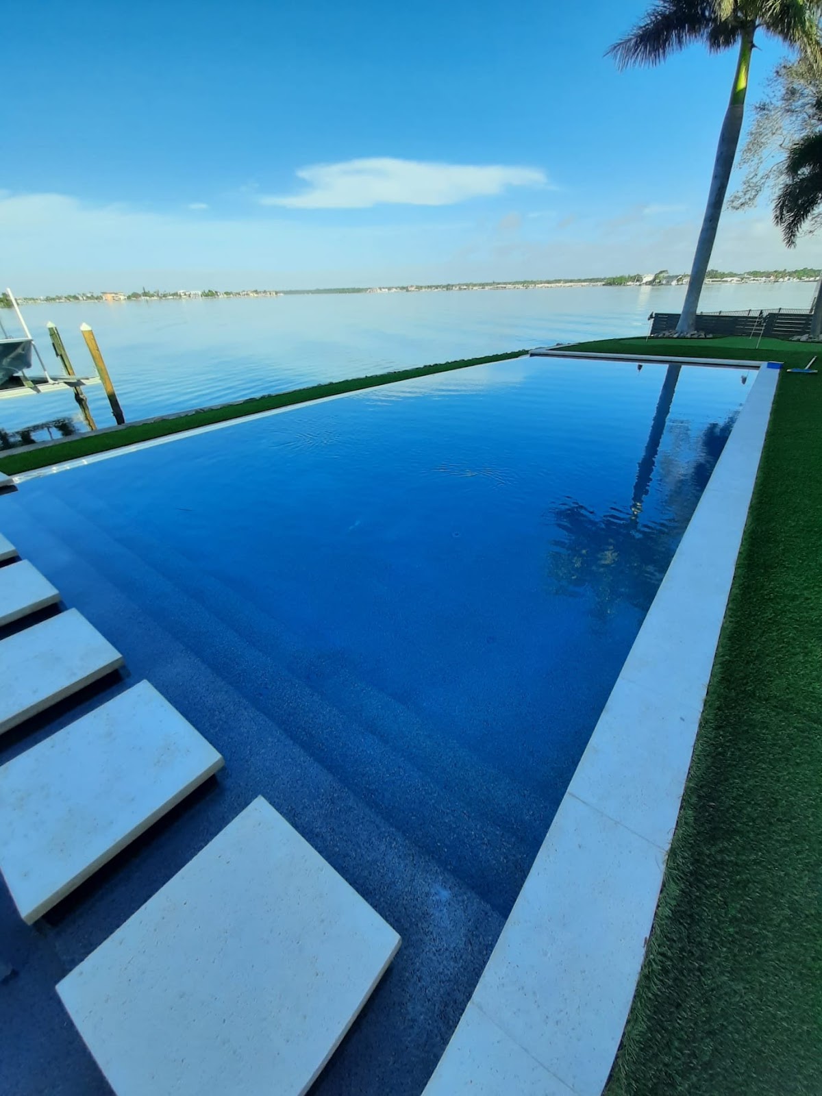 Modern infinity-edge swimming pool overlooking a waterfront view, with dark blue water, clean lines, and tropical surroundings.