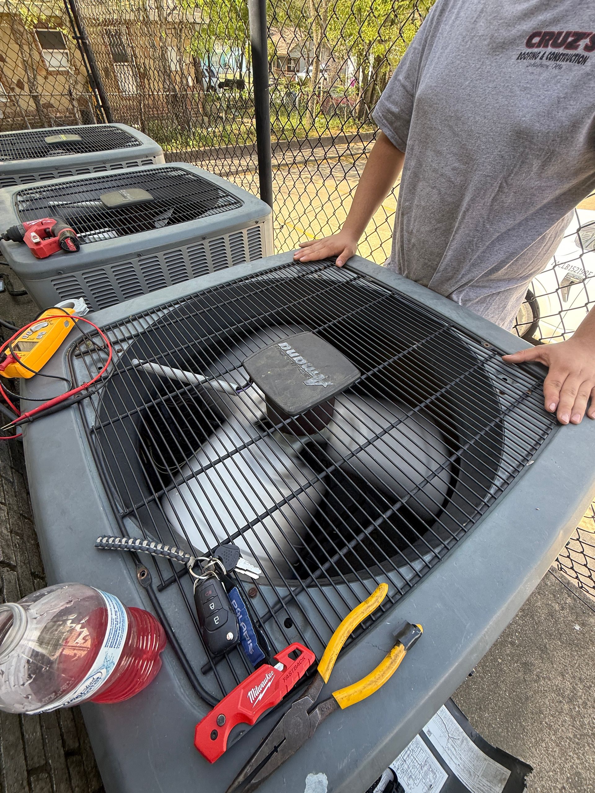 Technician working on outdoor condenser fan with tools placed on top. Multiple units aligned, indicating maintenance or repair service on residential HVAC systems, focusing on airflow and cooling performance.