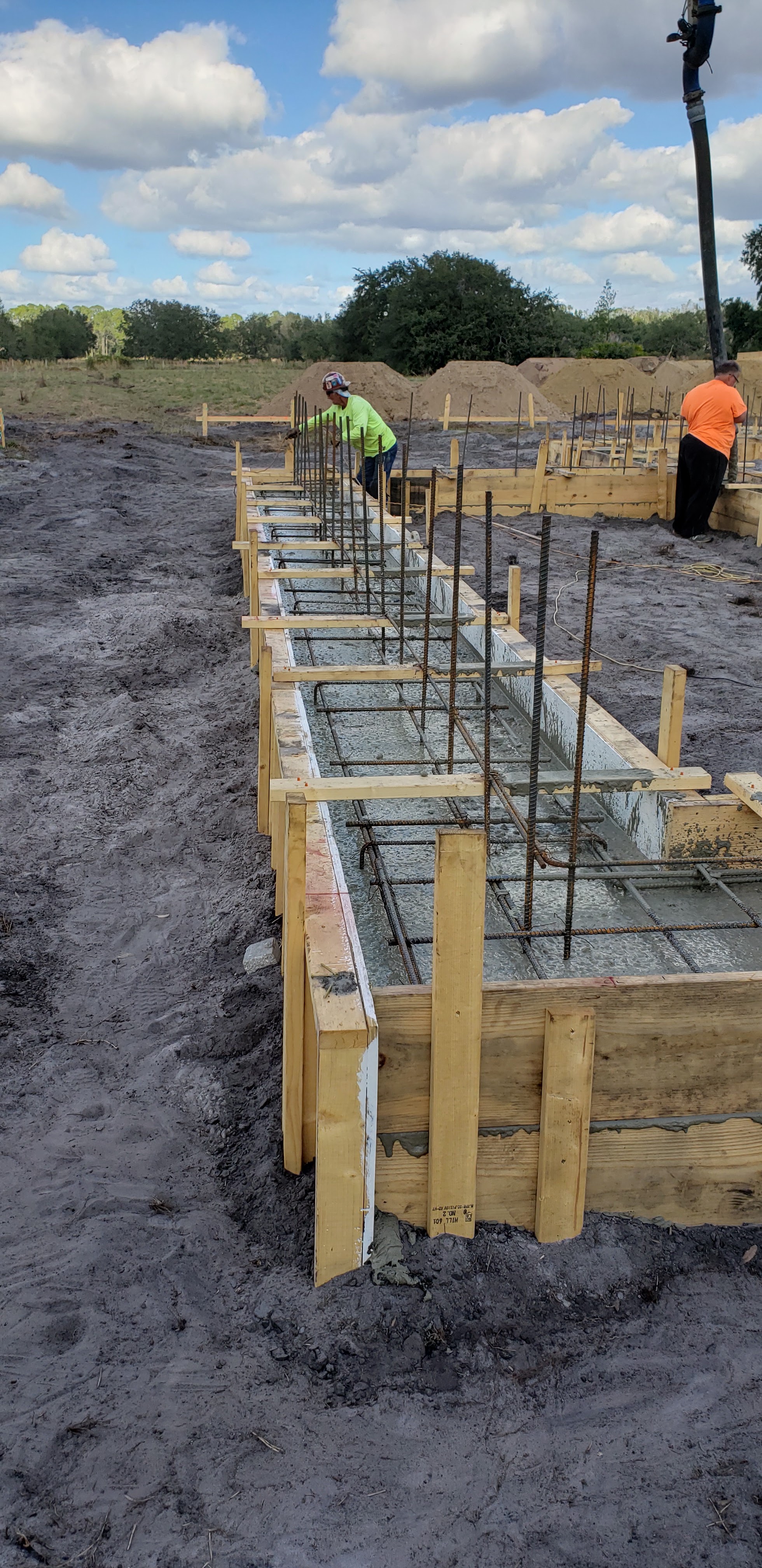 Construction workers are pouring concrete into a foundation form made of wood and rebar. The scene t 