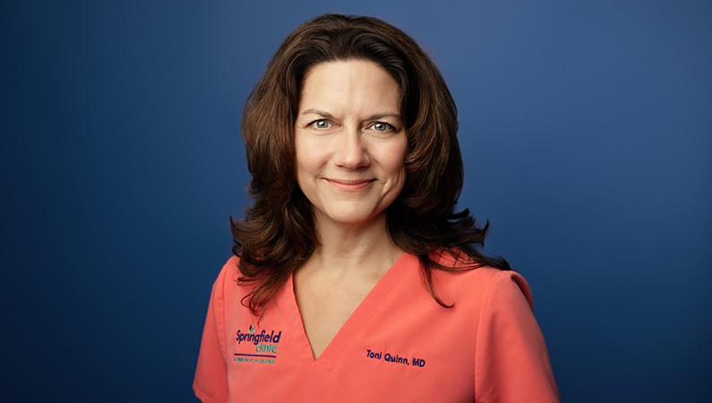 Female physician smiling in front of blue photo backdrop.