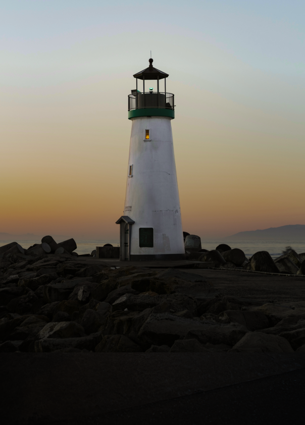 A lighthouse on a rocky oceanside outpost, pictured at dusk.