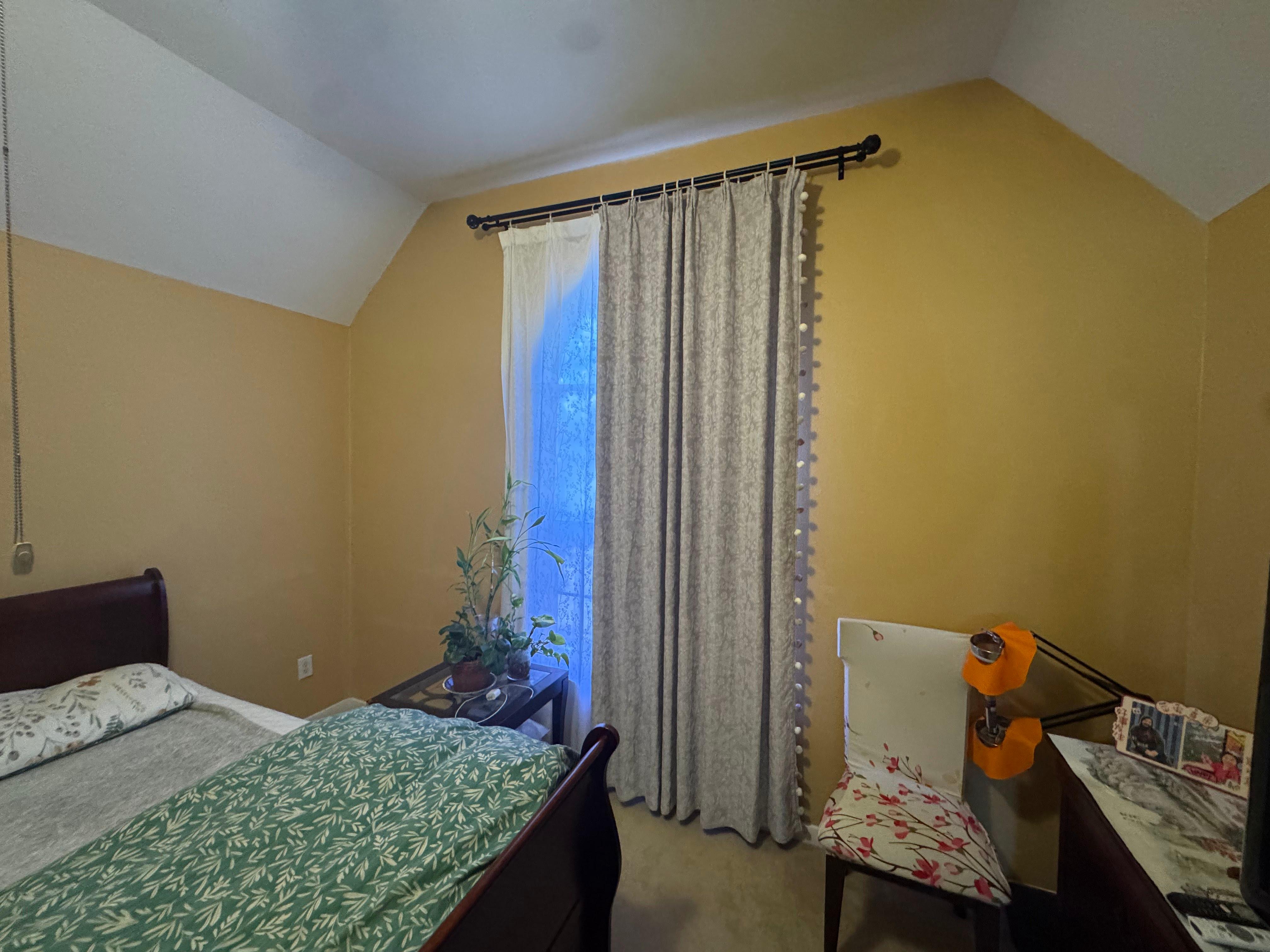 Textured curtain panels installed on a black curtain rod over a tall bedroom window.