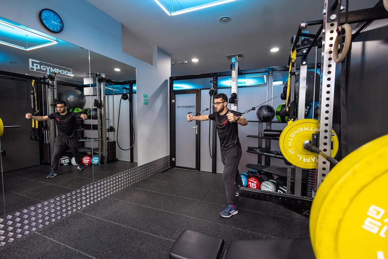 Man using cable machine for chest exercise in a private strength pod at GYMPODS Putney with squat rack and mirrored wall.