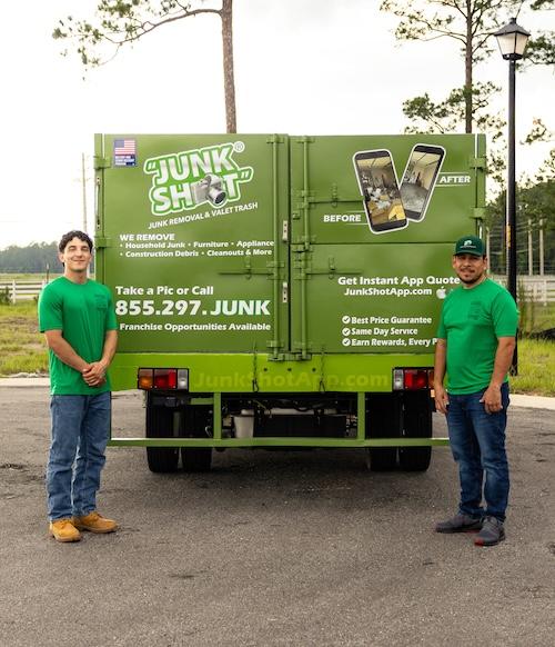 Two male crew members in matching green Junk Shot t-shirts and jeans standing proudly in front of th 