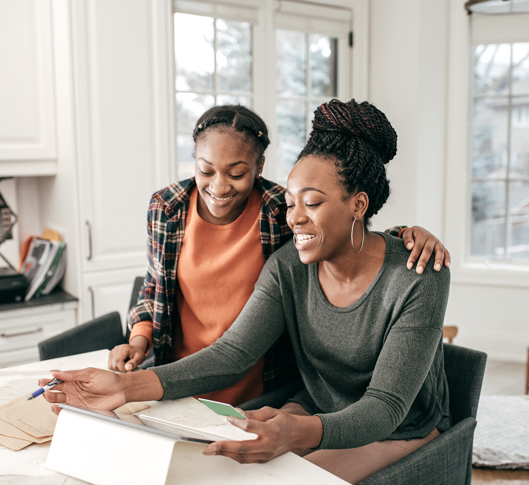 A mother and daughter looking over documents on an iPad in their kitchen.