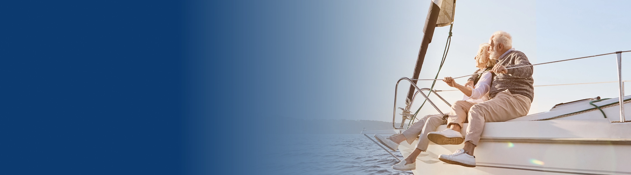 An elderly couple sitting on the bow of a boat with their legs hanging down.