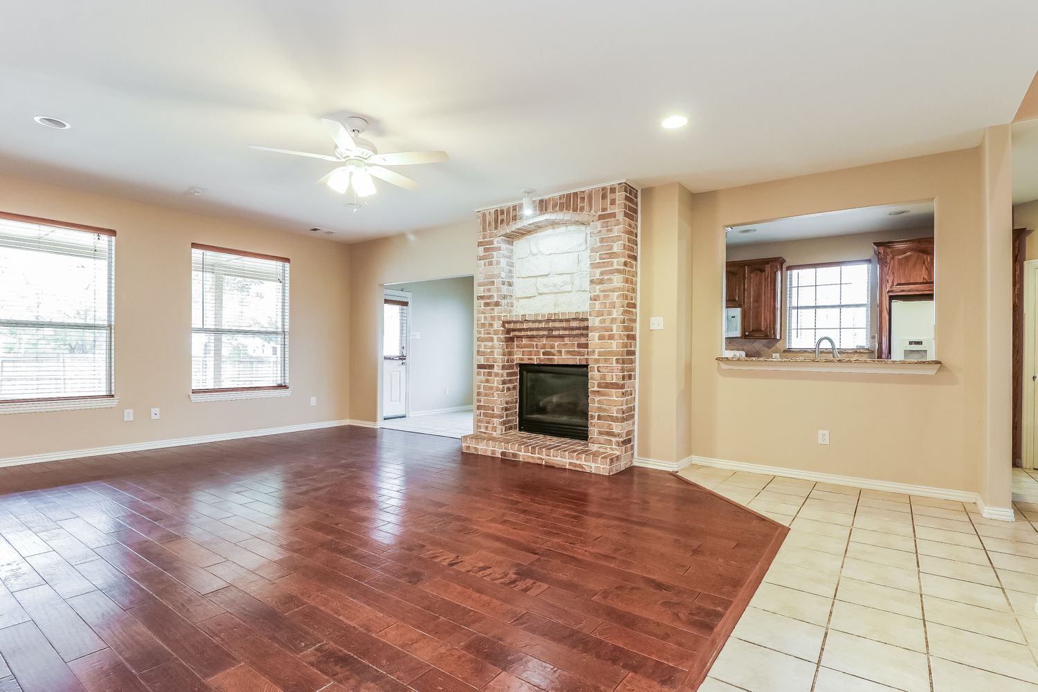 Family room with fireplace and wood flooring with window peering into kitchen at Invitation Homes Dallas.