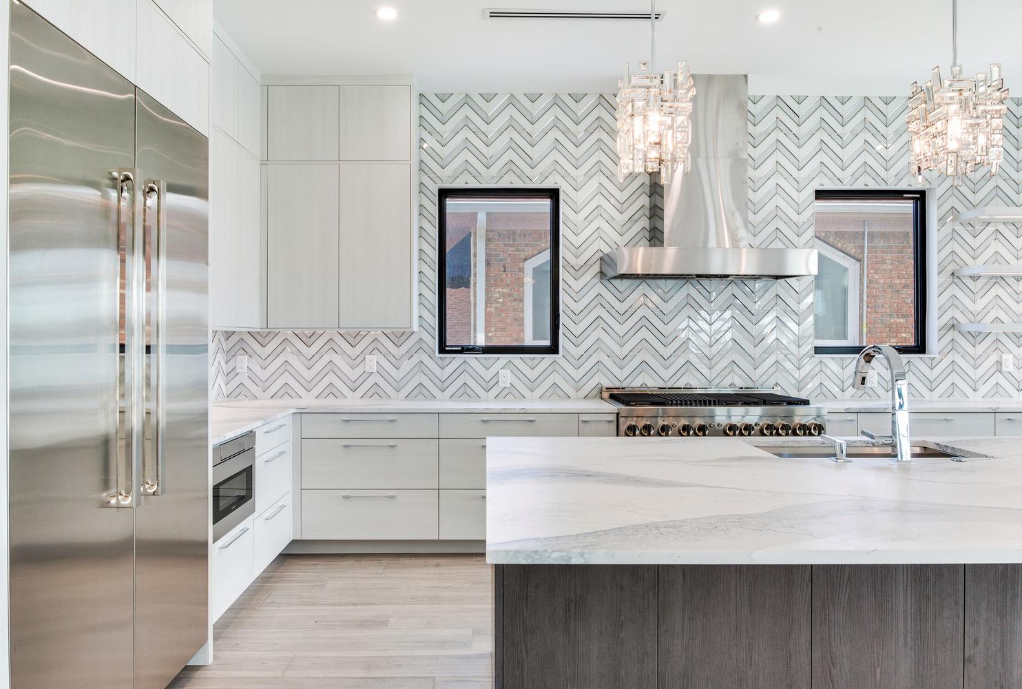 Elegant primary bathroom with a double vanity, illuminated mirrors, decorative tile wall, glass shower, and modern luxury fixtures.