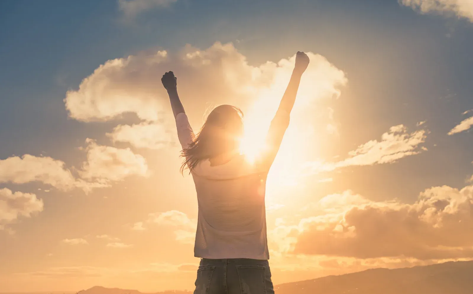 The image shows a person with arms raised against a bright sky with clouds. The sun shines behind them, creating a silhouette. The scene conveys a sense of triumph and freedom.