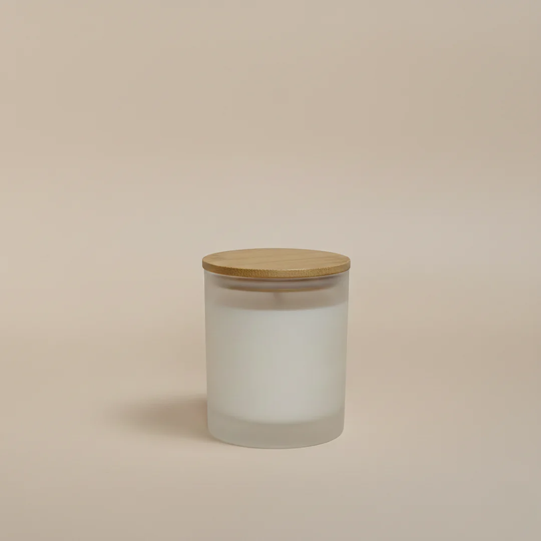 A frosted glass jar candle with a bamboo lid sits centered against a plain, light tan background. The candle appears to be unlit and filled with white wax.