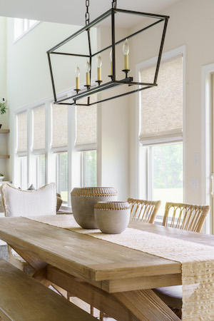 These cream-woven wood shades elegantly enhance the ambiance of this dining room. As the daylight filters through these shades, they effortlessly brighten the area, making it a welcoming and charming setting to eat with your family!