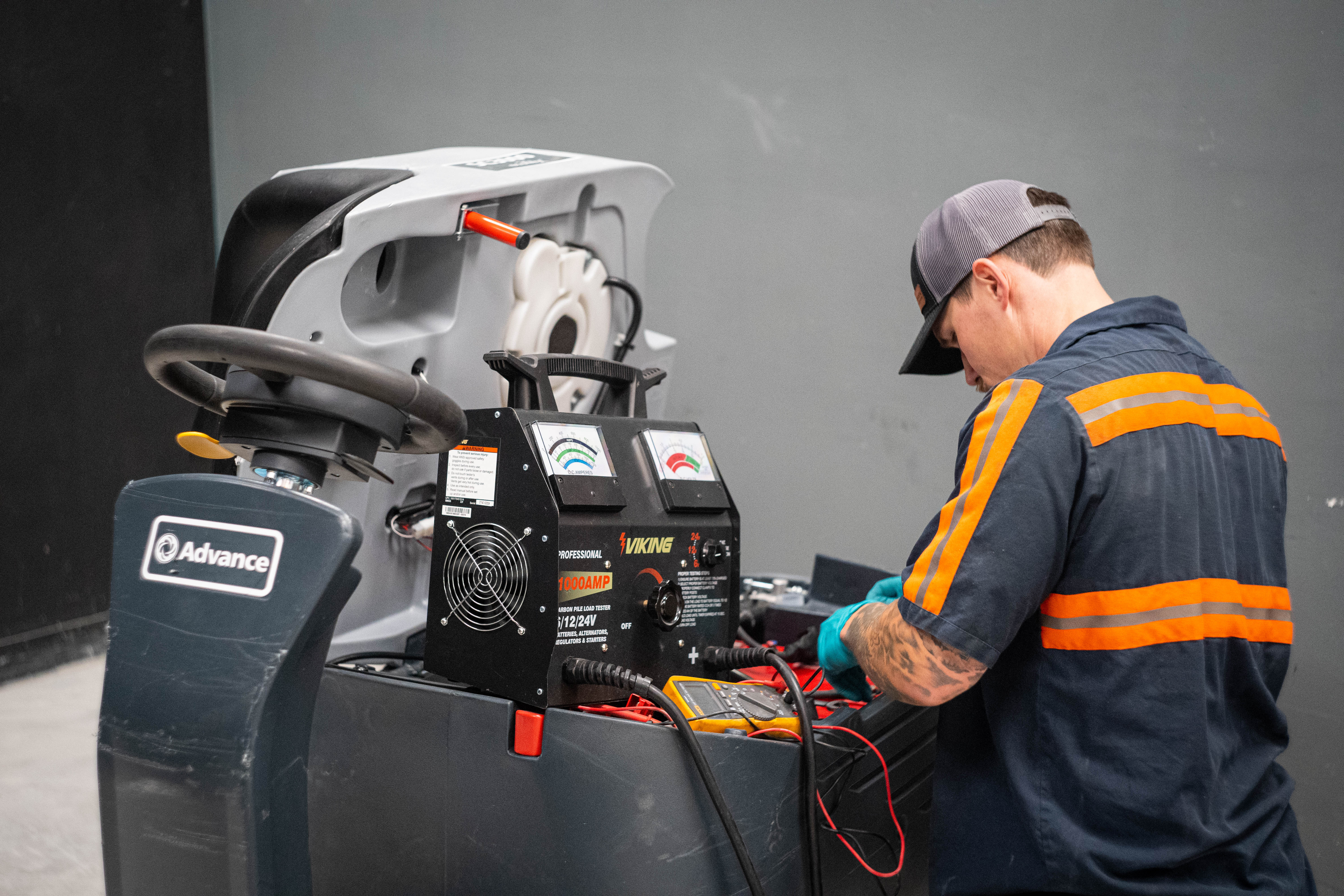 A WaySolutions expert technician performs a heavy-duty battery load test on an Advance commercial ride-on floor scrubber. Utilizing a professional Viking 1000-amp carbon pile load tester, the technician evaluates the voltage drop and capacity of the machine's deep-cycle battery bank. This vital preventative electrical service helps Layton supermarkets and industrial facilities avoid unexpected downtime in their high-capacity cleaning fleets.