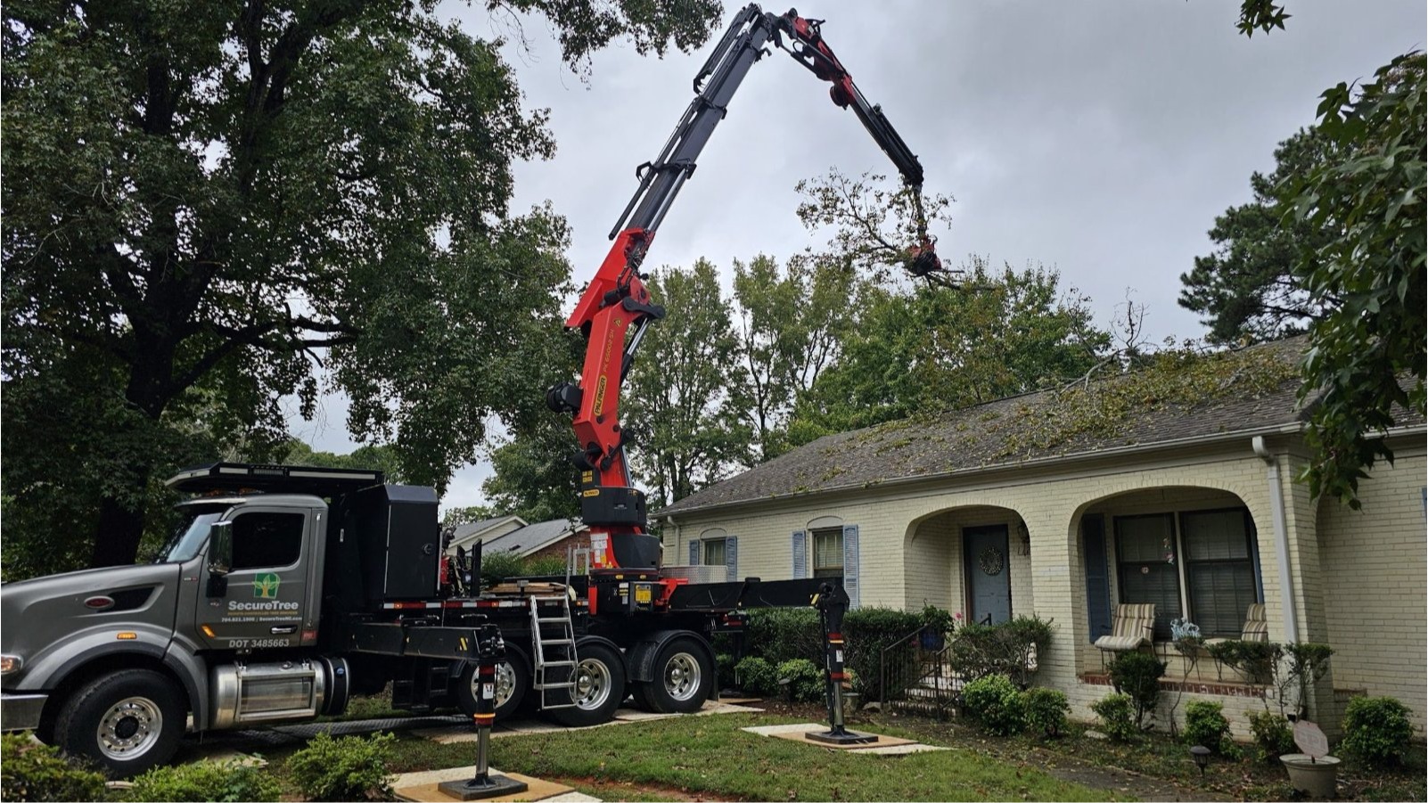 Knuckleboom crane removing a large tree beside a house in Indian Trail, NC