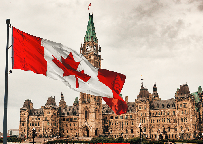 A Canadian flag waving in front of the Parliament building in Ottawa.