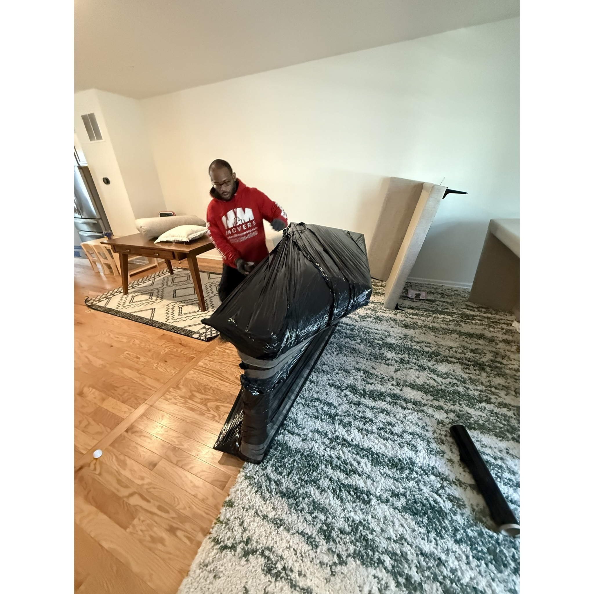M&M Movers team member finishing protective shrink-wrap on a large upholstered furniture piece, keeping it secure and scratch-free before loading for the move.