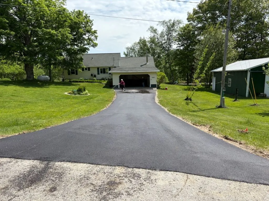 Newly paved residential asphalt driveway leading to a suburban home with neatly maintained lawn, clean edges, and smooth blacktop surface.