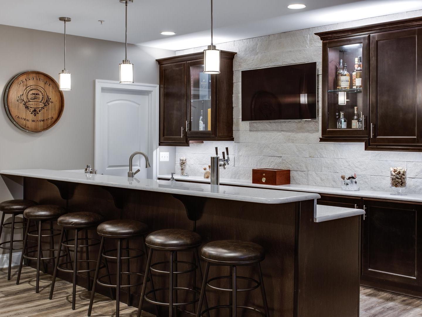 A wet bar design in a dark espresso cabinet finish features nicely in a finished game room or basement area.  The more seats the merrier!