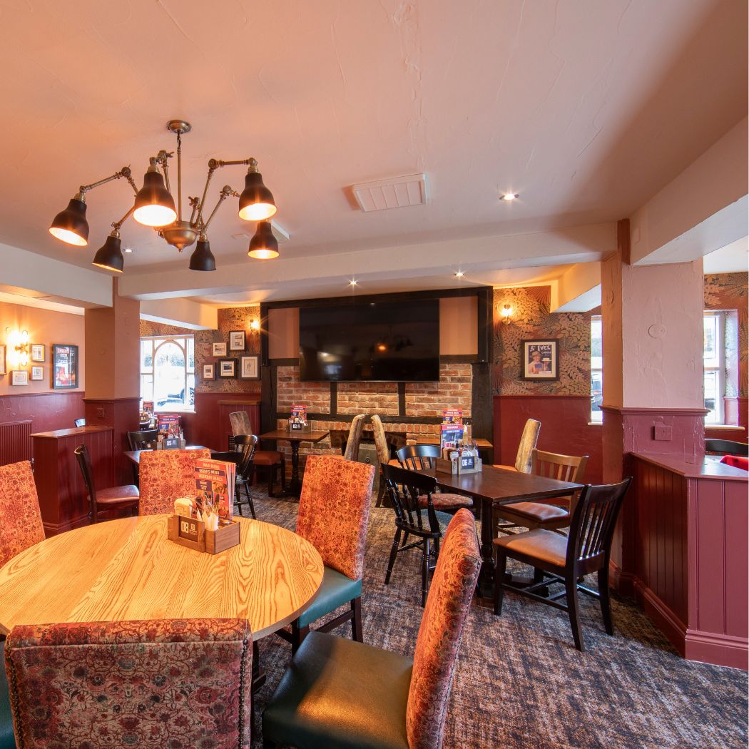 Comfortable seating area at The Arrow with dining tables, upholstered chairs and warm lighting, ideal for relaxed meals and everyday visits.