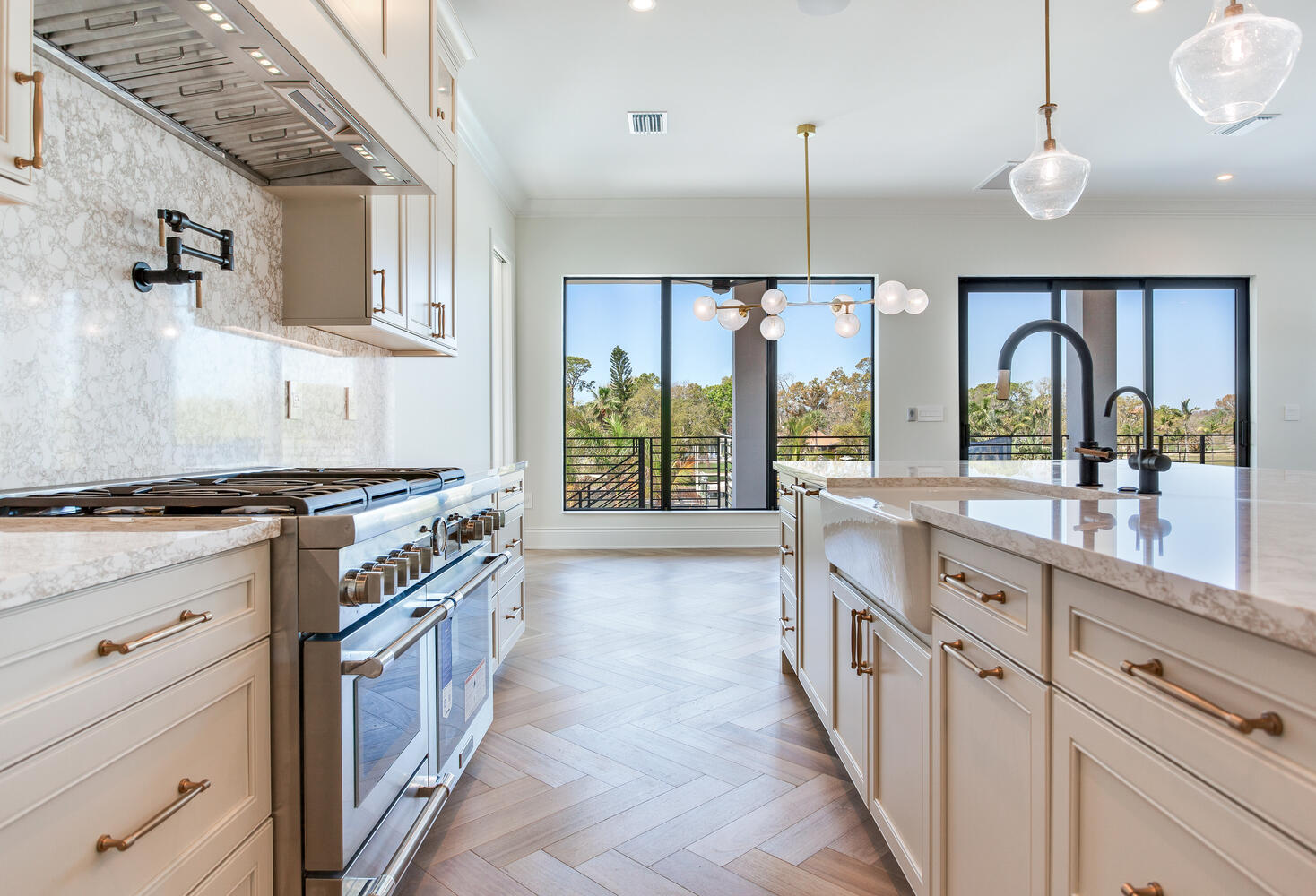 Bright coastal kitchen with custom cabinetry, pendant lighting, stainless appliances, wood flooring, and sliding glass doors leading outdoors.