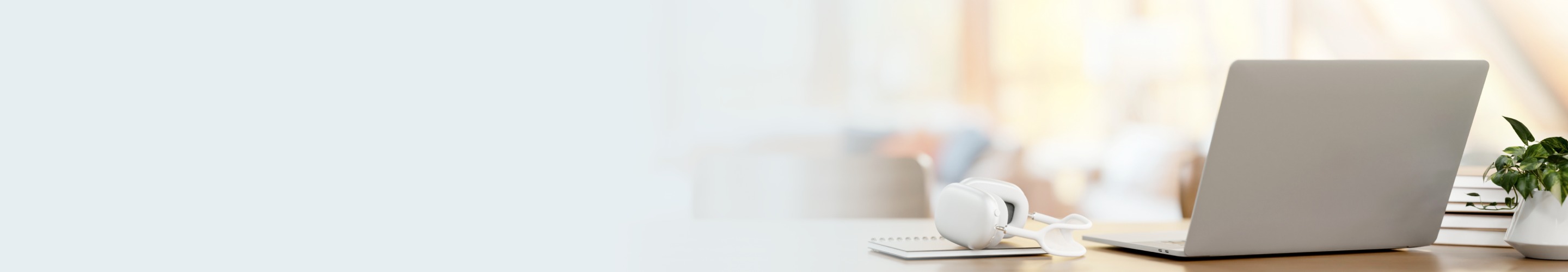 Desk with notebooks, a laptop, headphones, and a potted plant.
