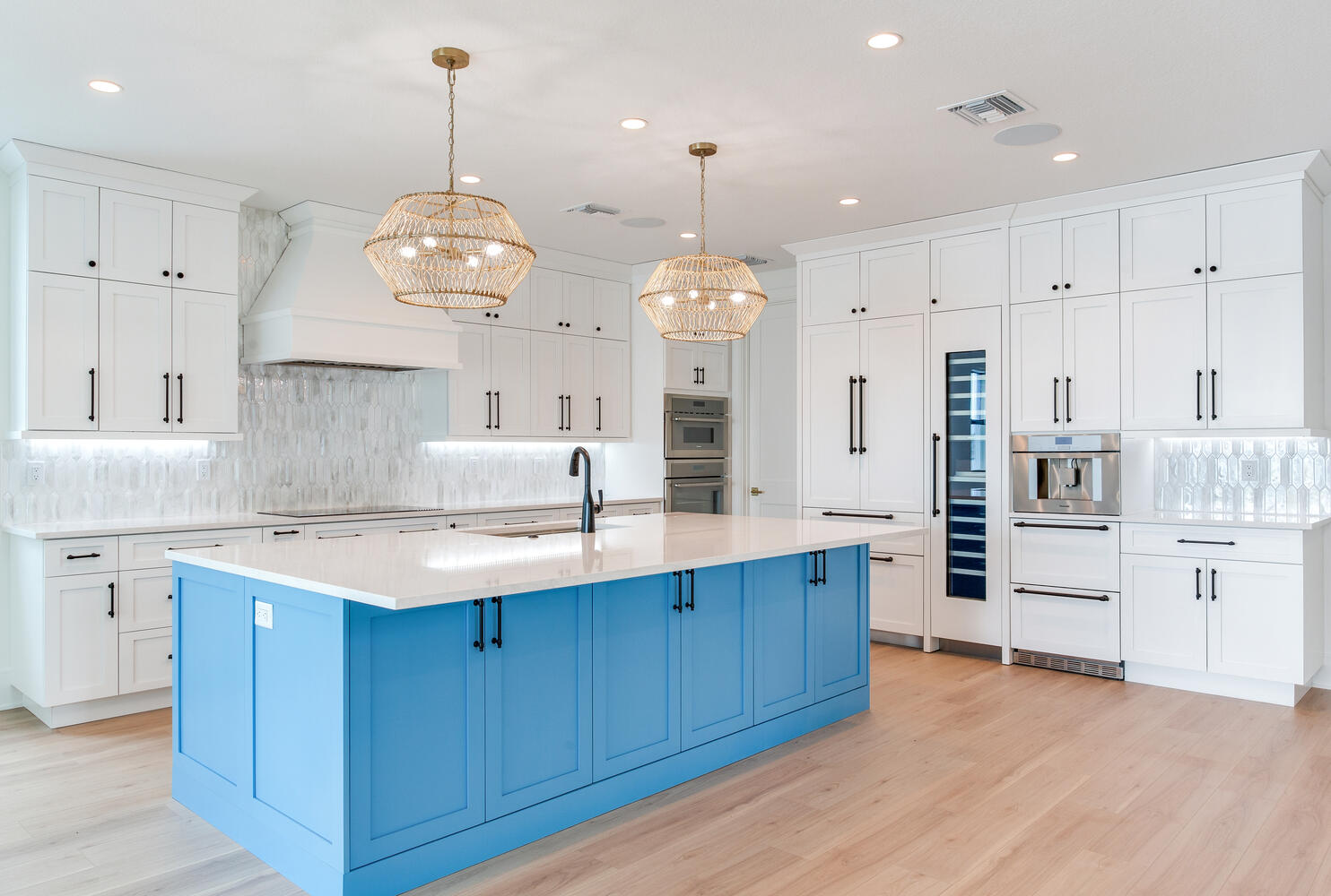 Custom AVENTIS kitchen featuring a vibrant blue island, white shaker cabinets, elegant pendant lighting, stainless appliances, and upscale coastal finishes.
