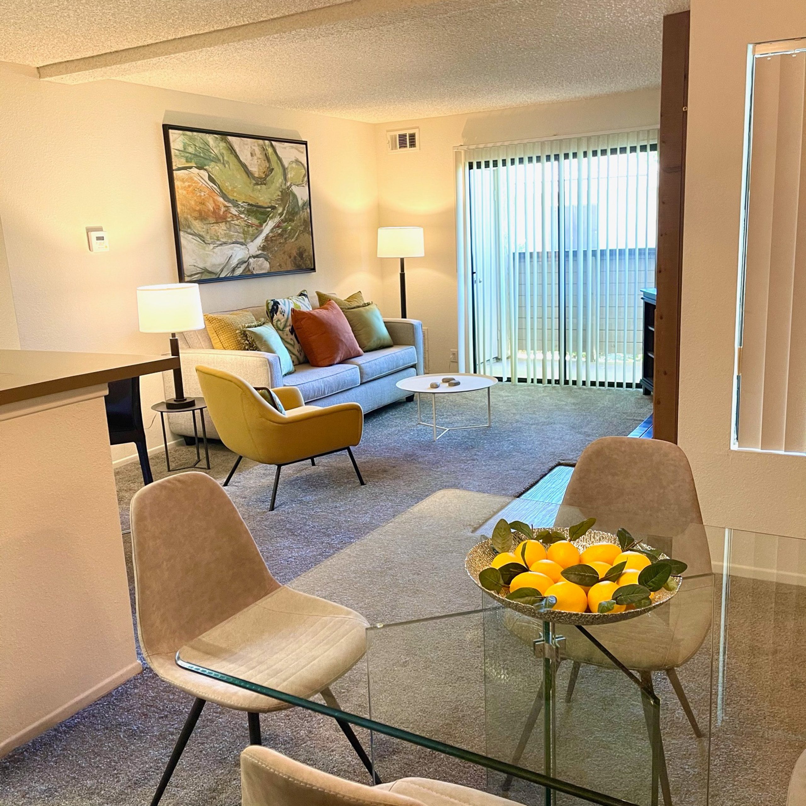 A living room with a yellow chair and a glass table.