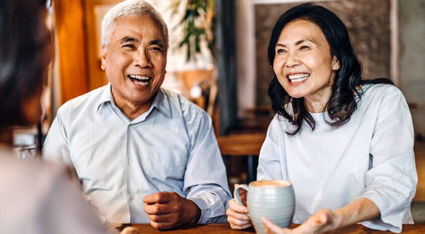 A happy couple discusses Medicare coverage options with an insurance agent over coffee in their home.