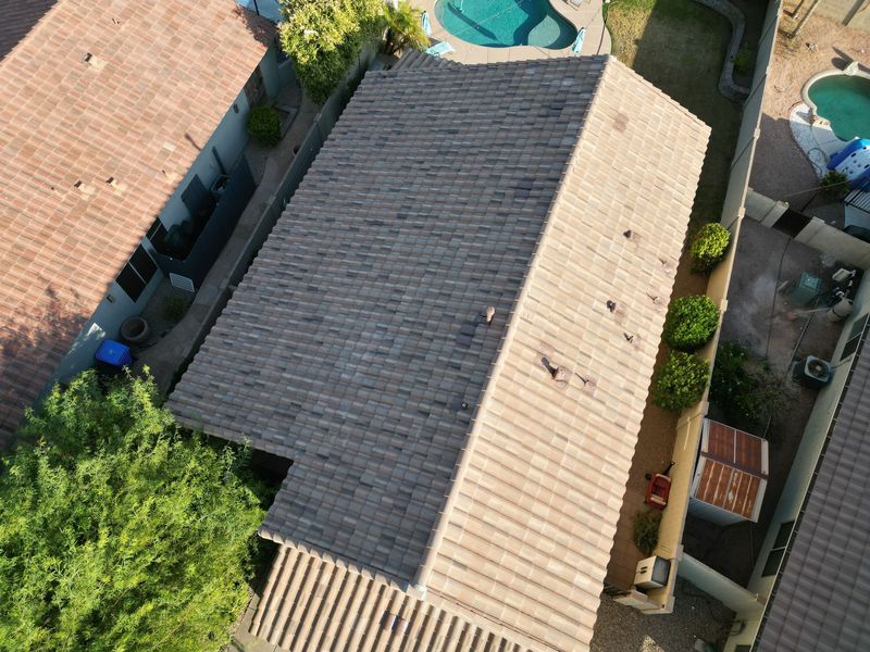 High-angle aerial drone view of a finished residential roofing project. The image highlights a clean, uniform installation of tan and gray concrete tiles on a suburban home with a backyard pool.