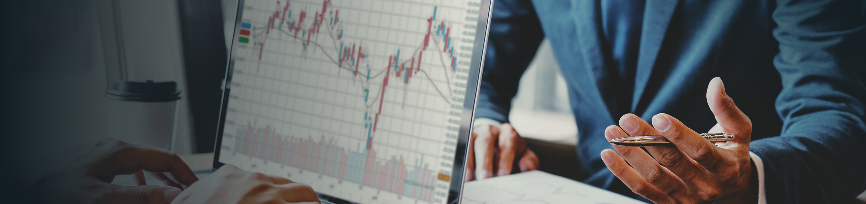 Close up of two people in a business meeting, one with an open laptop featuring charts and graphs, and the other writing in a notebook.