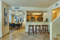 Tiled kitchen and dining areas with lighting, bar with view to kitchen, and three bar stools.