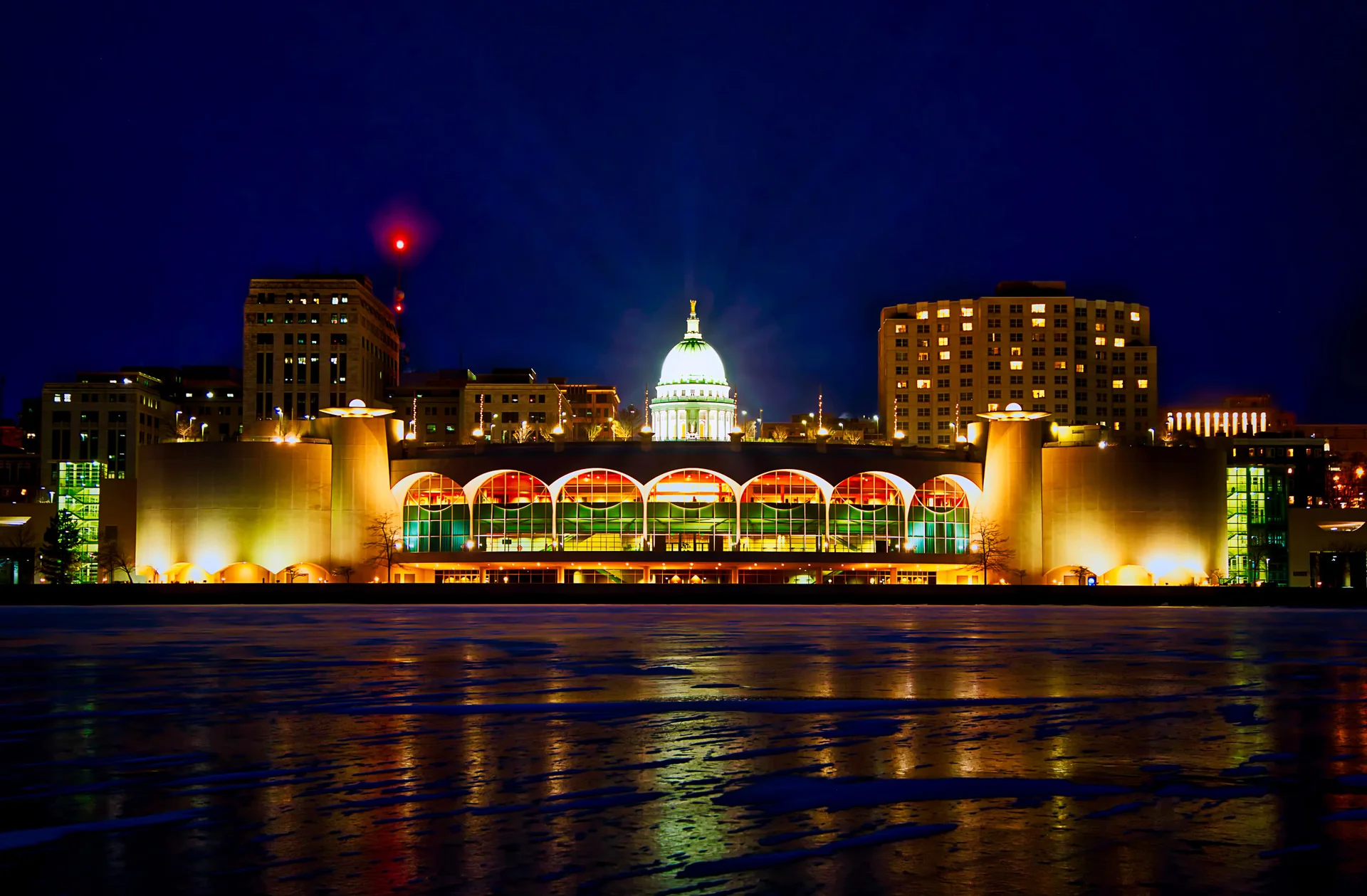 Madison’s illuminated skyline and Wisconsin State Capitol glow above frozen Lake Monona in this striking winter nightscape captured by Bob Hundt Photography, with vibrant reflections across the ice.