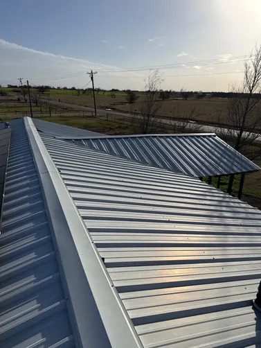 A newly installed standing seam metal roof provides durable weather protection, clean architectural lines, and long-lasting performance while overlooking surrounding rural landscapes under bright daylight conditions.