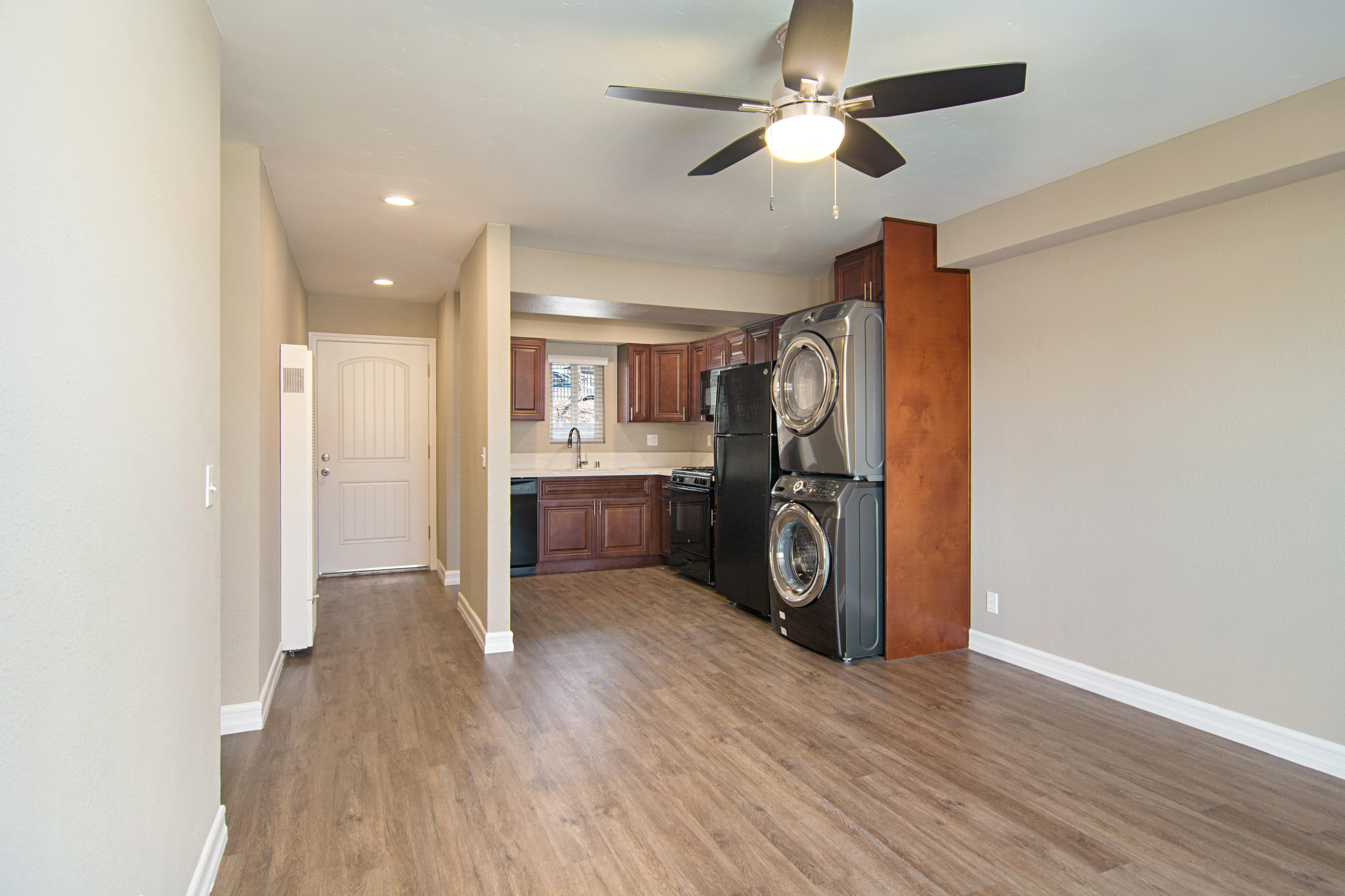 Living room and kitchen with wood-style floors, ceiling fan, and stackable washer-dryer