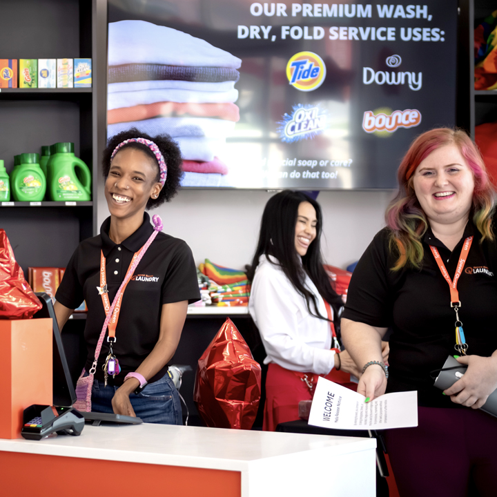Friendly Speed Queen Laundry team members welcoming customers from behind the service counter. 