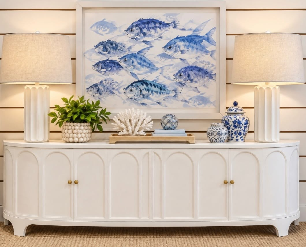 A curved white sideboard, matching lamps, blue fish artwork, and decorative jars create a coastal look at True Fashionistas. Discover secondhand furniture and home decor for a new look with character.