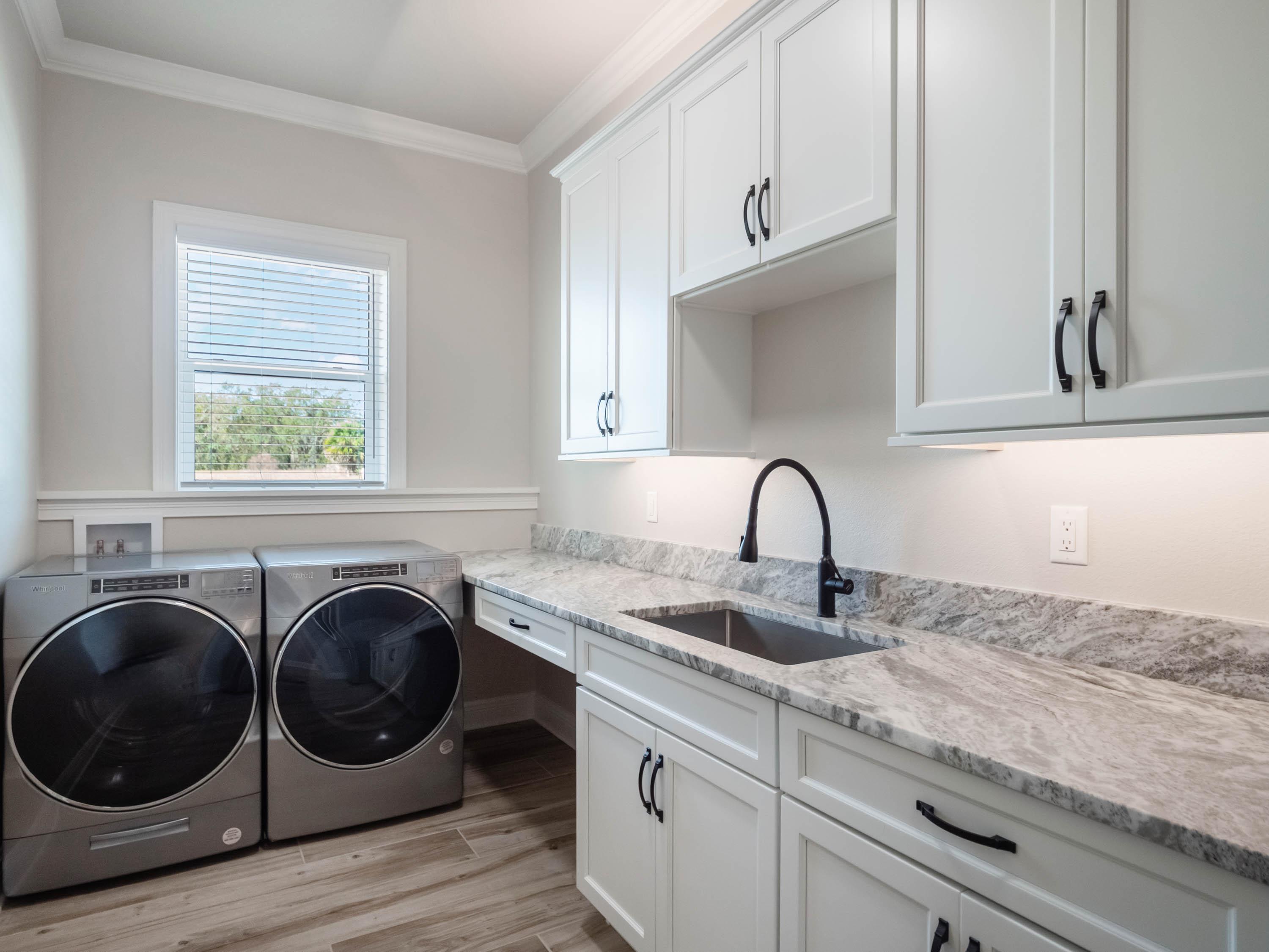 Custom laundry room in a luxury Central Florida home featuring white shaker cabinets, quartz countertops, utility sink, and built-in storage designed by custom home builders in Central Florida.
