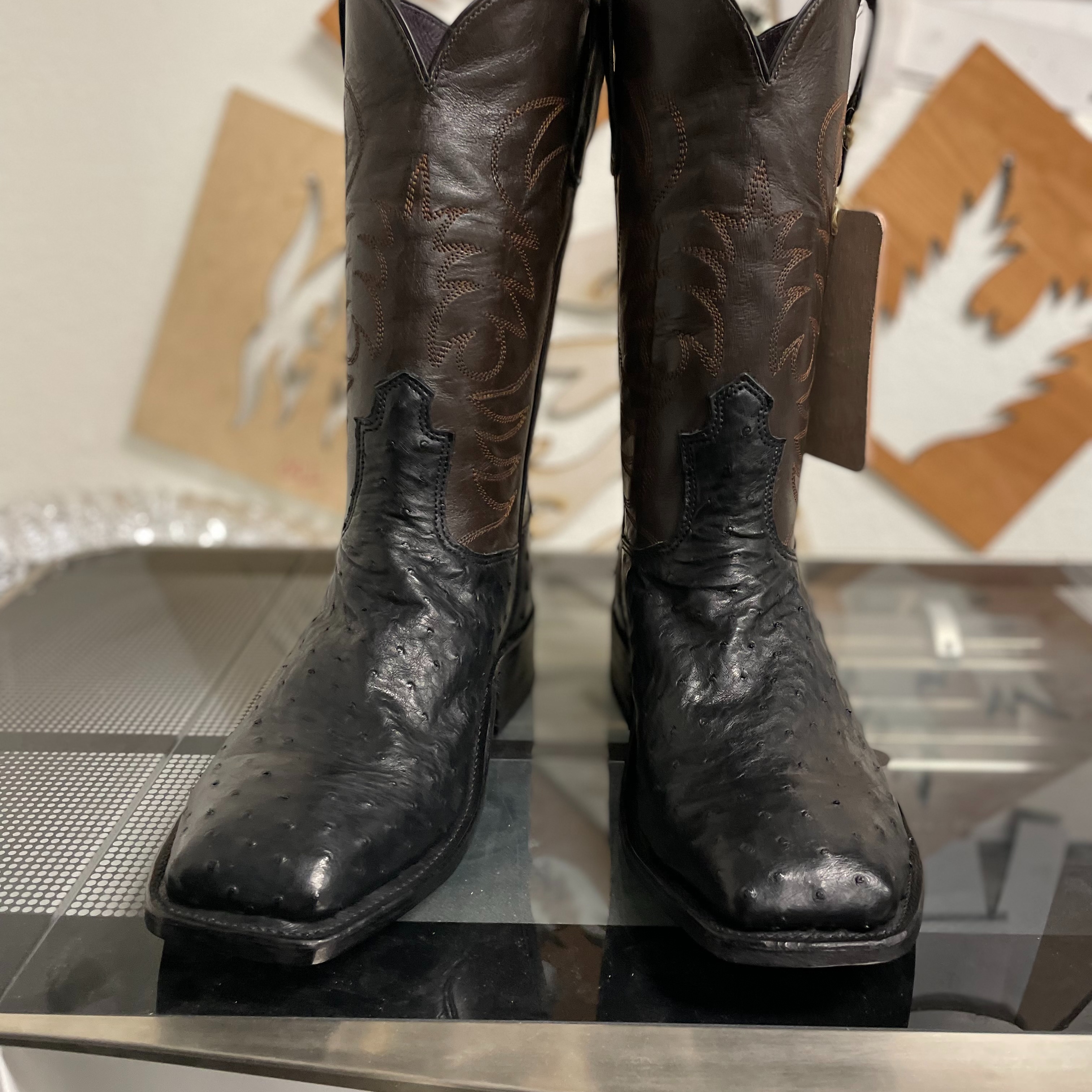 A pair of black custom cowboy boots featuring textured leather, brown Western stitching, and square  