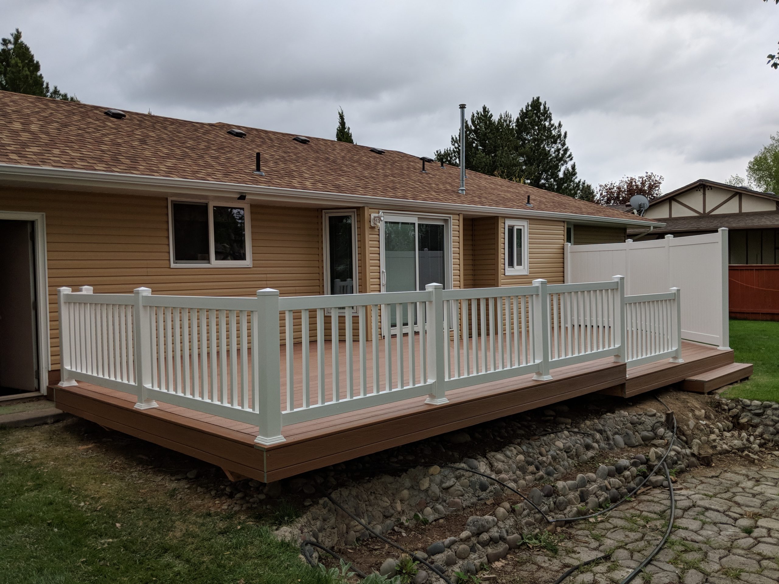 Create a beautiful and durable outdoor living space with a custom composite deck from DeckPro LLC. This project pairs rich brown composite decking with clean white vinyl railing for a classic, low-maintenance look that perfectly complements the home's siding and provides a great space for relaxation.
