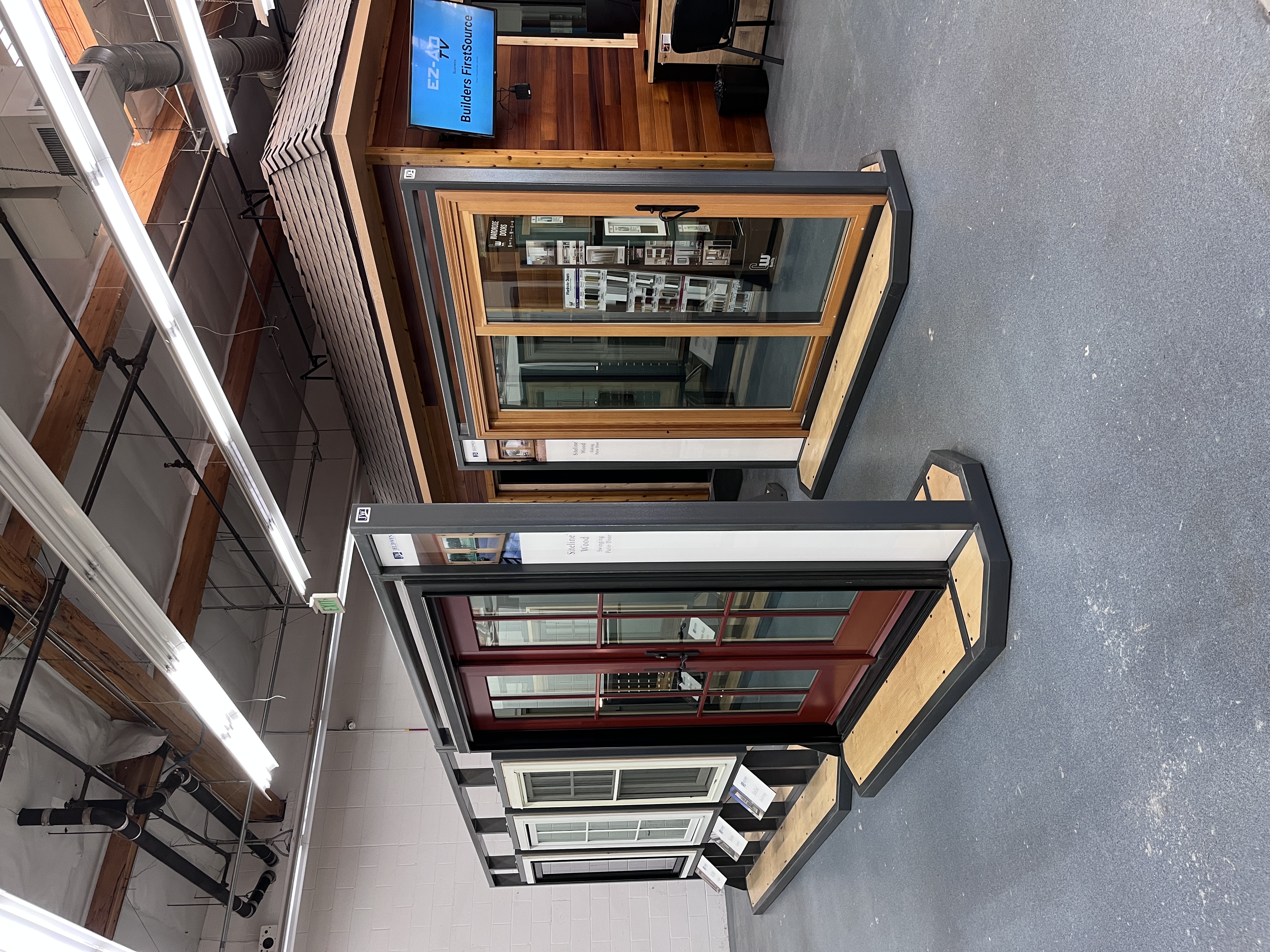 JELD-WEN Siteline Wood window and patio door showroom display at Builders FirstSource Thousand Oaks, CA, featuring a red swinging French door and a wood-tone sliding door in front of a mock house structure.