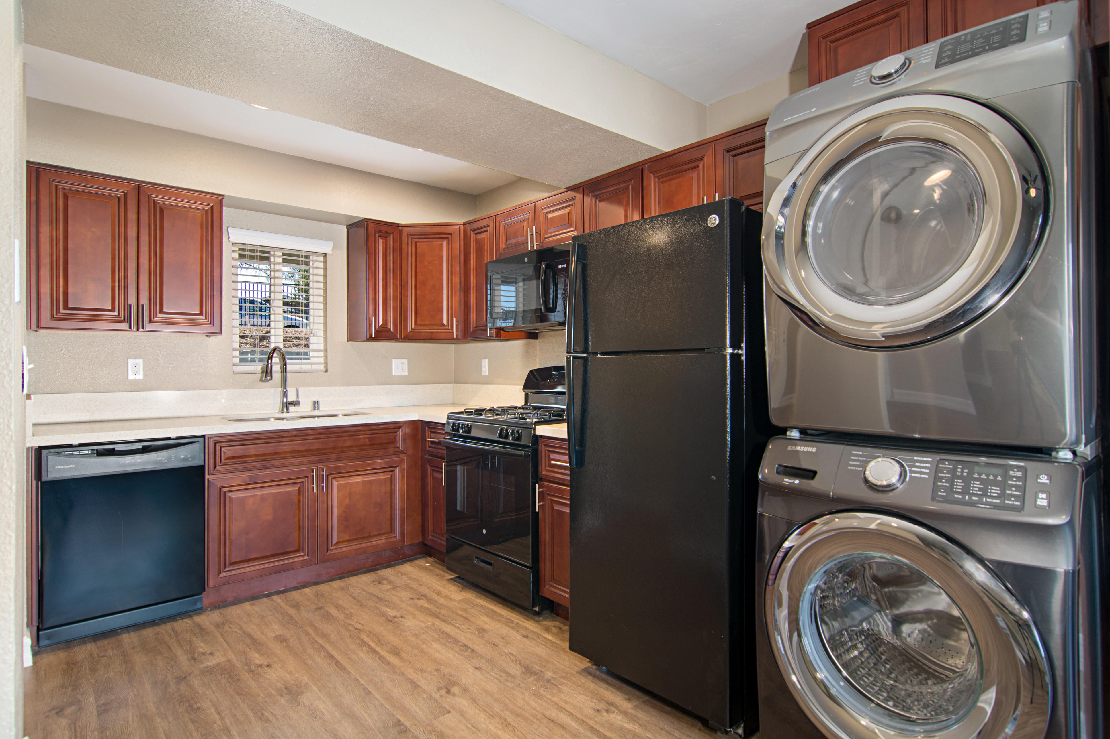 Kitchen with black appliances, maple cabinets, plank flooring, and full-size washer and dryer.