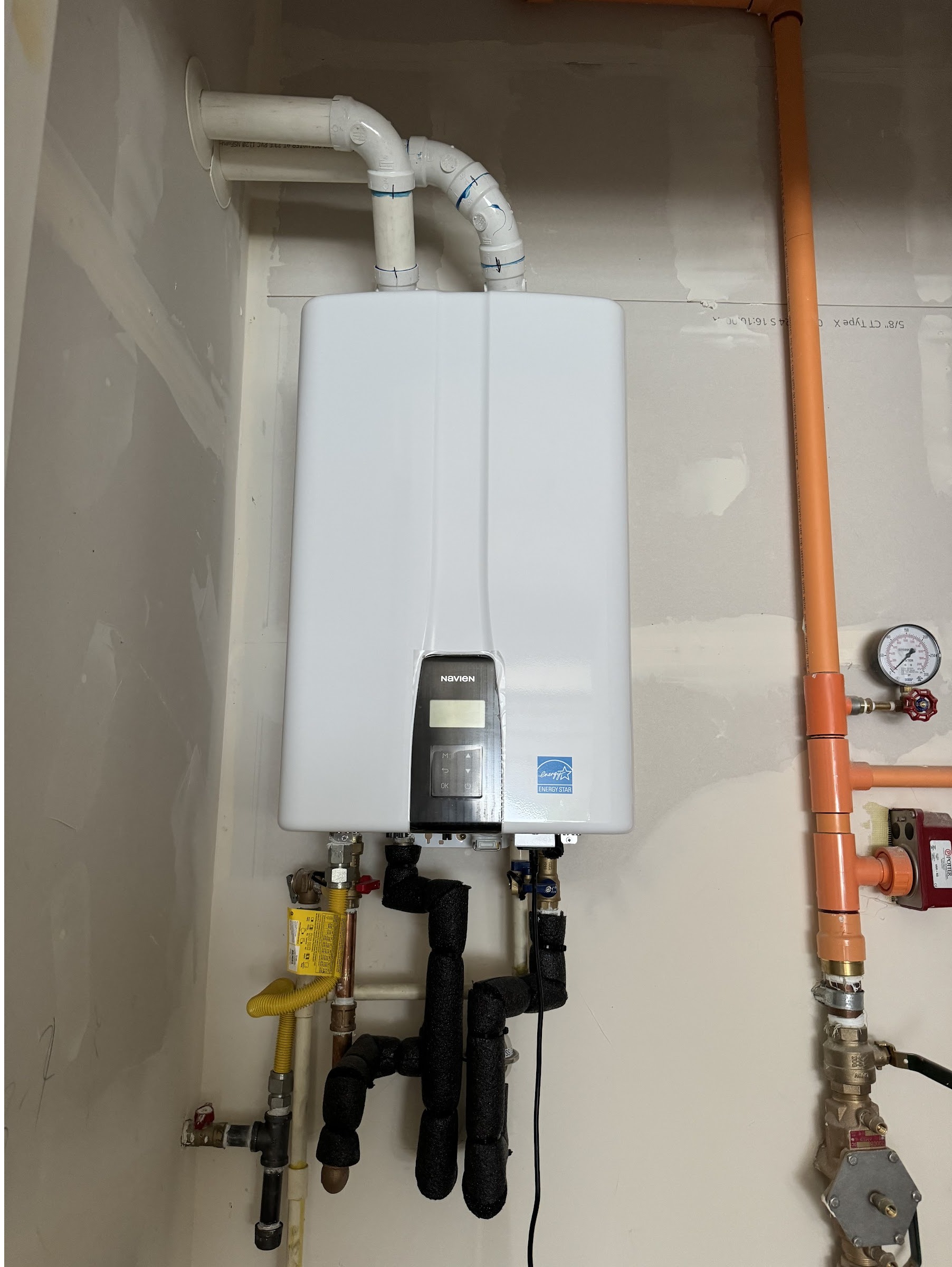 Finished tankless water heater install with copper supply piping and a pressure gauge, by Ready Energy Solutions.